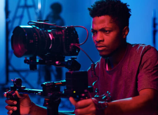 Cinematographer operating a professional camera rig on a film set with pink and blue lighting.