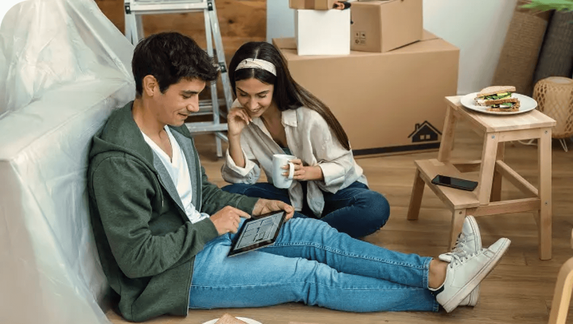 A man and woman sitting on the floor, focused on a laptop in front of them