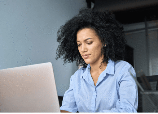 A woman with curly hair sits at a desk, focused on her laptop while working