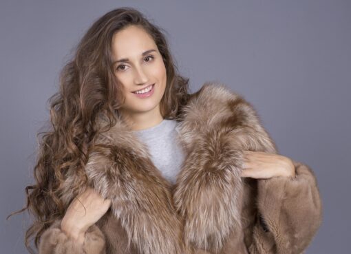A model wearing a long, luxurious black fur coat over a dark outfit. The coat has a soft, plush texture and a wide, oversized collar. The image captures the coat's elegance and length.